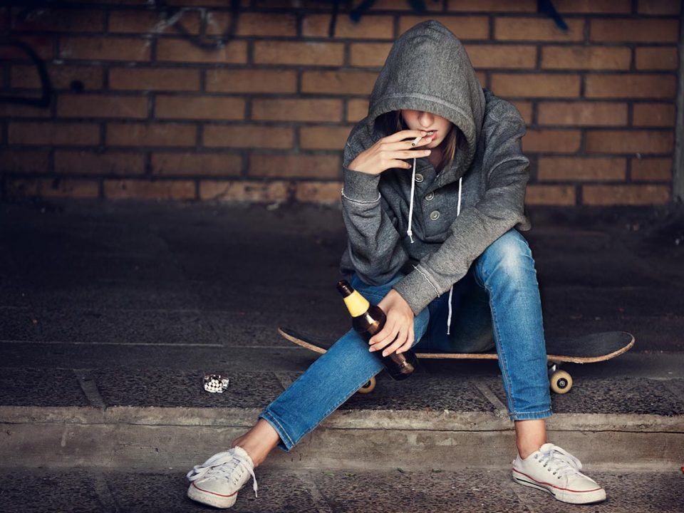 girl in a hoodie sitting on a skateboard smoking a cigarette