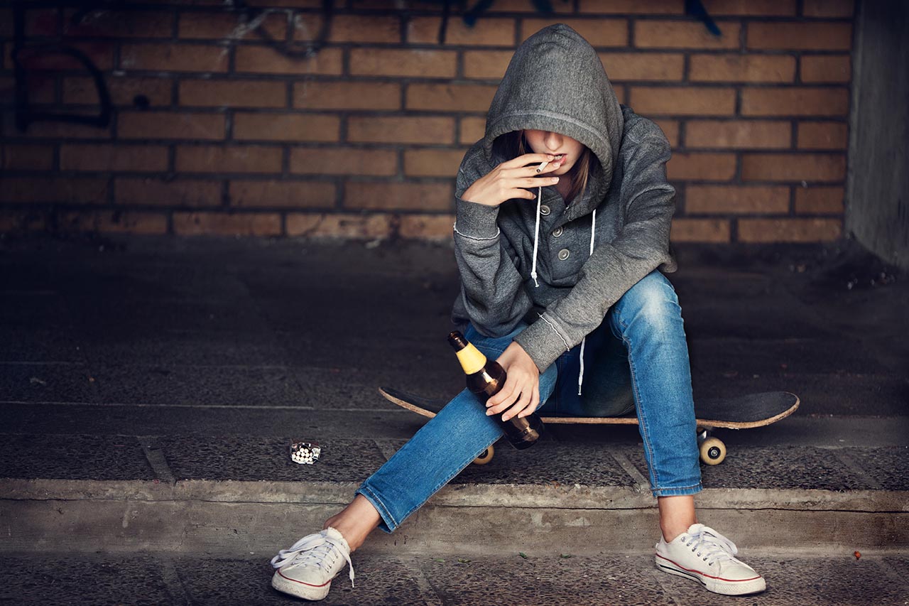 girl in a hoodie sitting on a skateboard smoking a cigarette